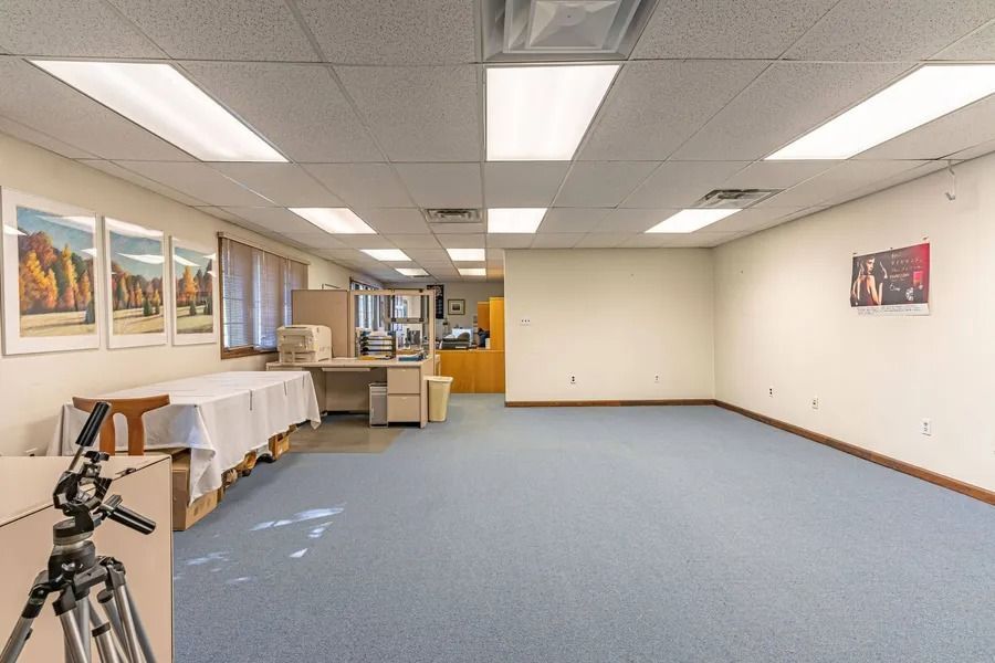 Empty office or meeting room with blue carpet, white walls, ceiling lights, and camera tripod in foreground