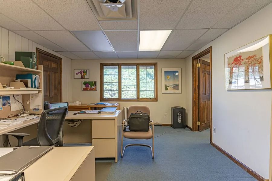 Empty office with desks, chairs, blue carpet, and a window at the back