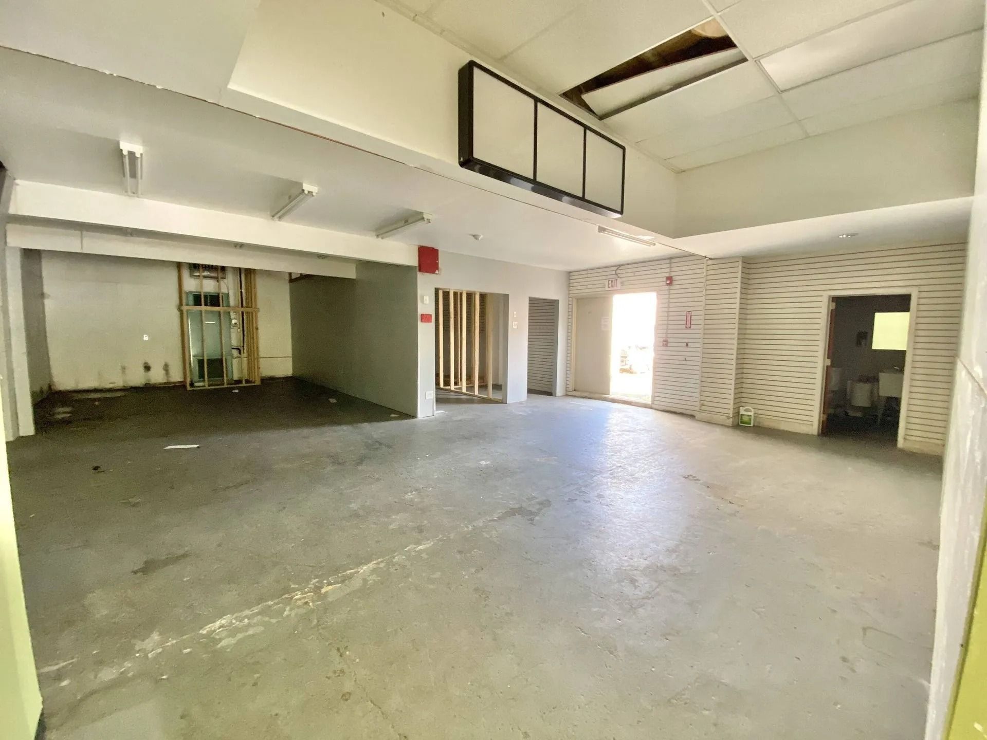 Empty concrete garage interior with white walls, open doorway, and fluorescent ceiling lights