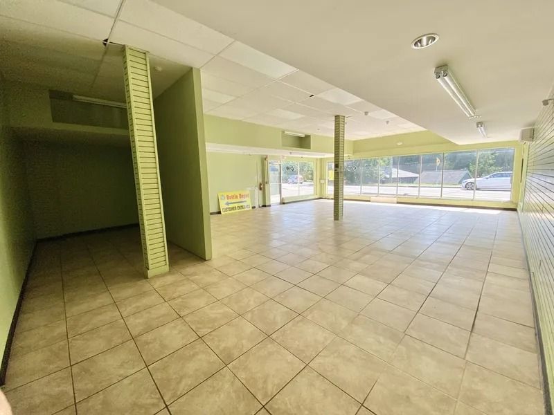 Empty tiled commercial space with green columns, large front windows, and bright natural light