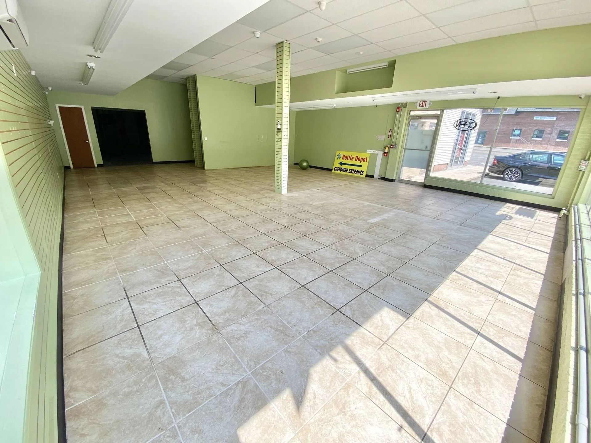 Empty tiled storefront interior with green walls and sunlight through the front windows