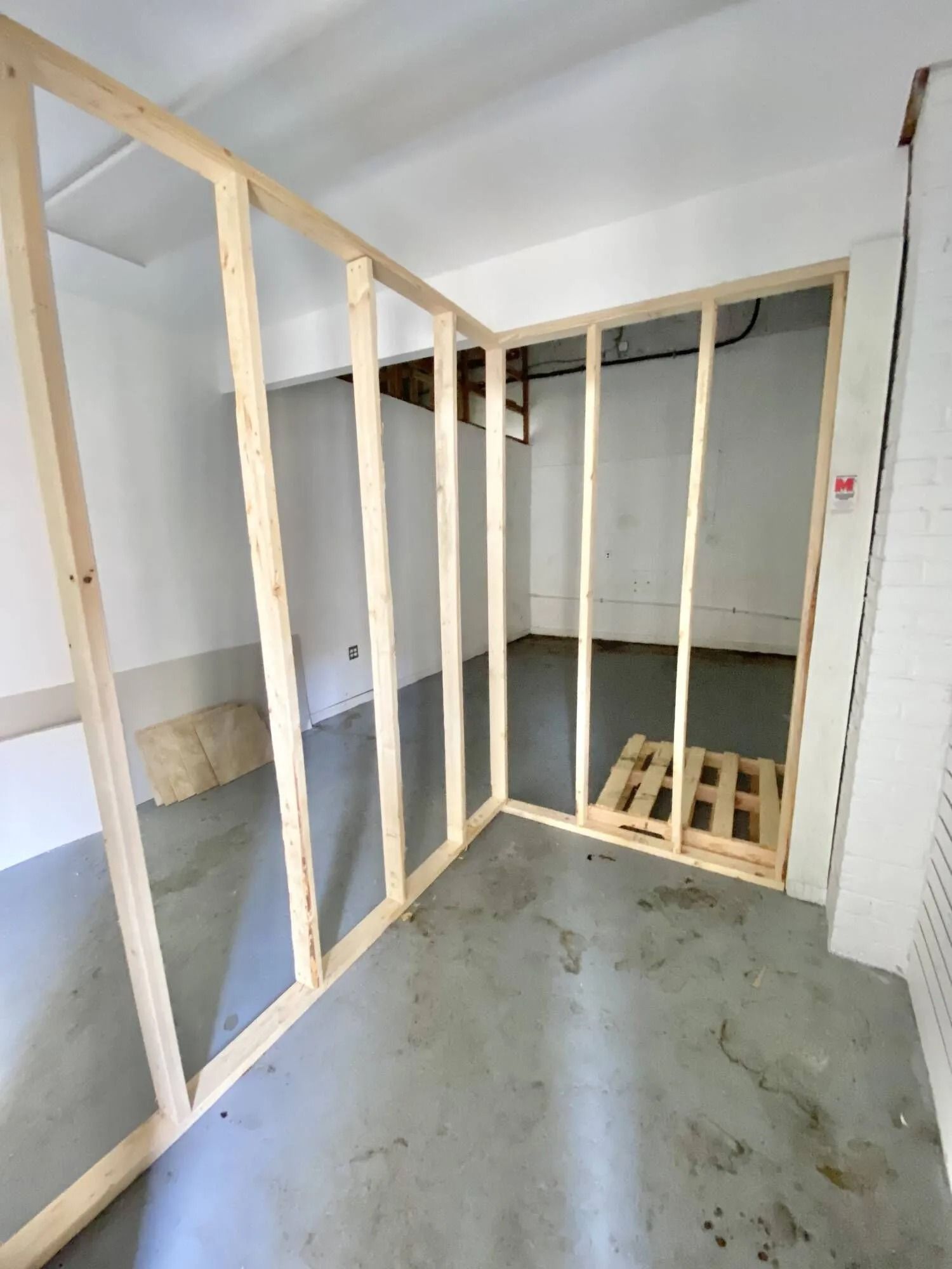 Unfinished room with exposed wooden wall framing, concrete floor, and a small stair opening at the back.