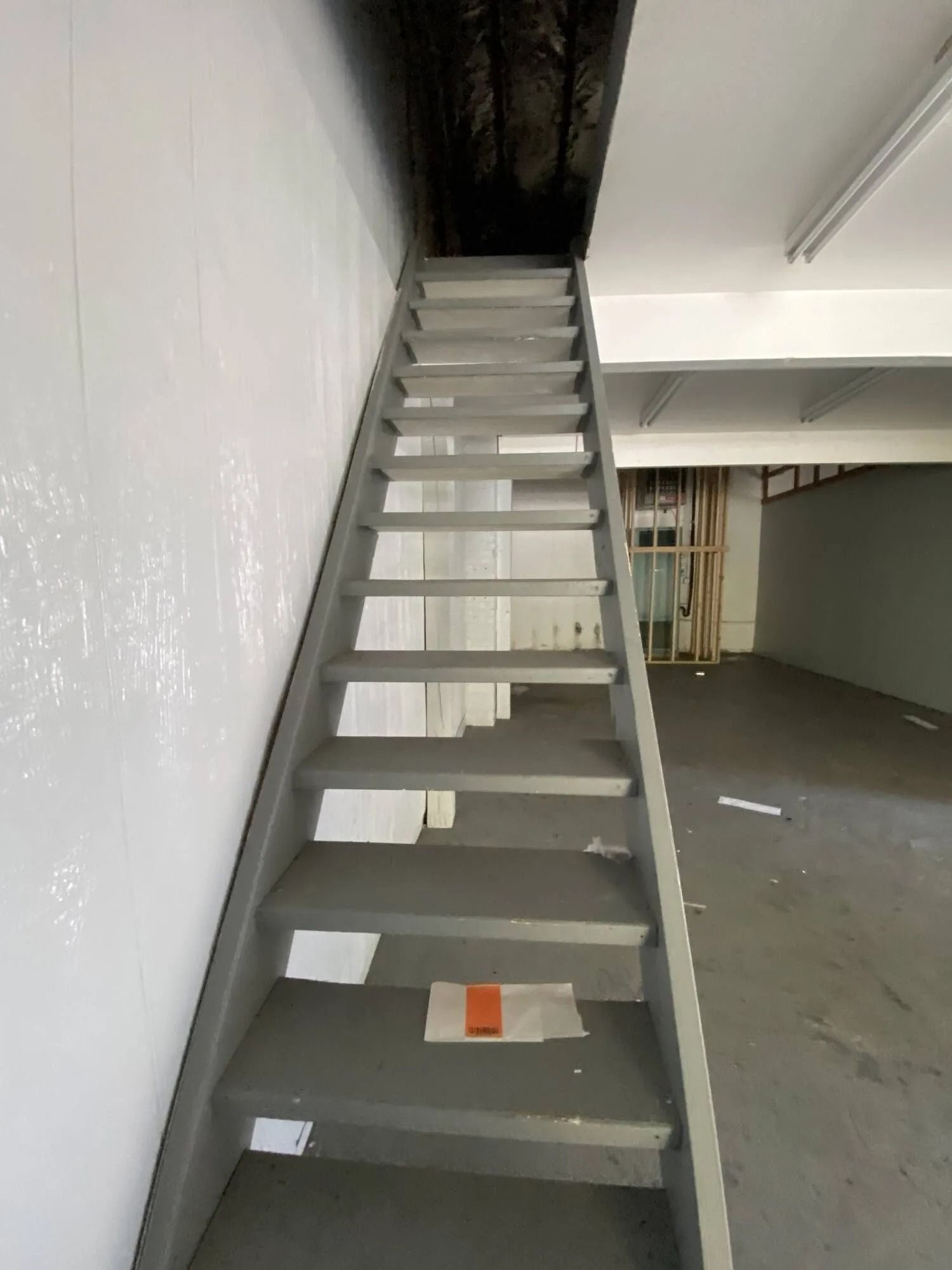 Metal ladder leading to a dark loft opening in an empty industrial room
