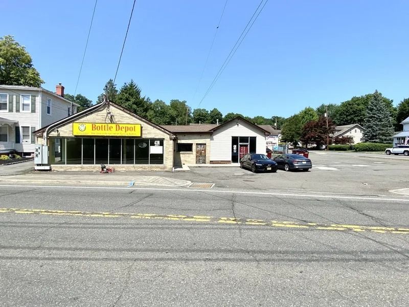 Small storefront with yellow sign beside a parking lot under a clear blue sky