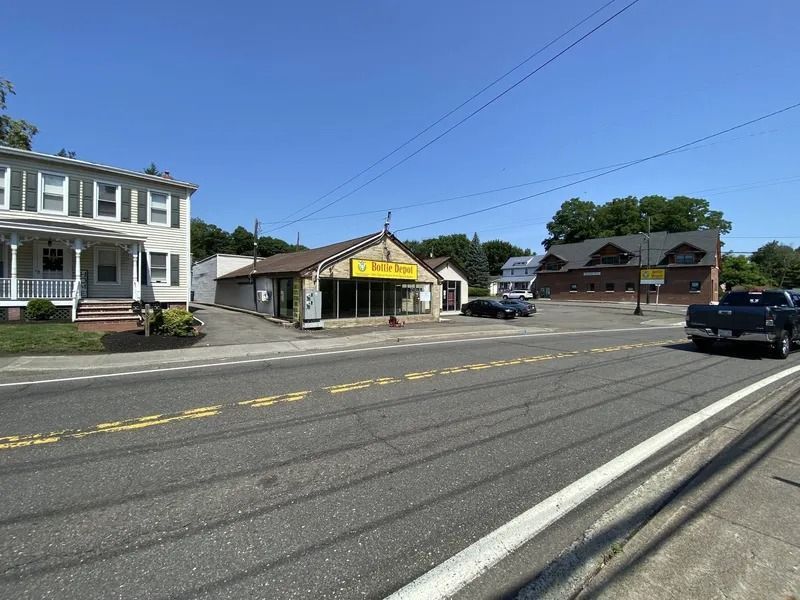 Small town street with storefronts, parked vehicles, and a white building under a clear blue sky