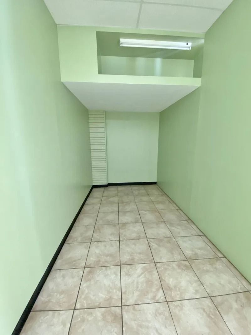 Narrow empty room with mint green walls, tiled floor, and a fluorescent light overhead.