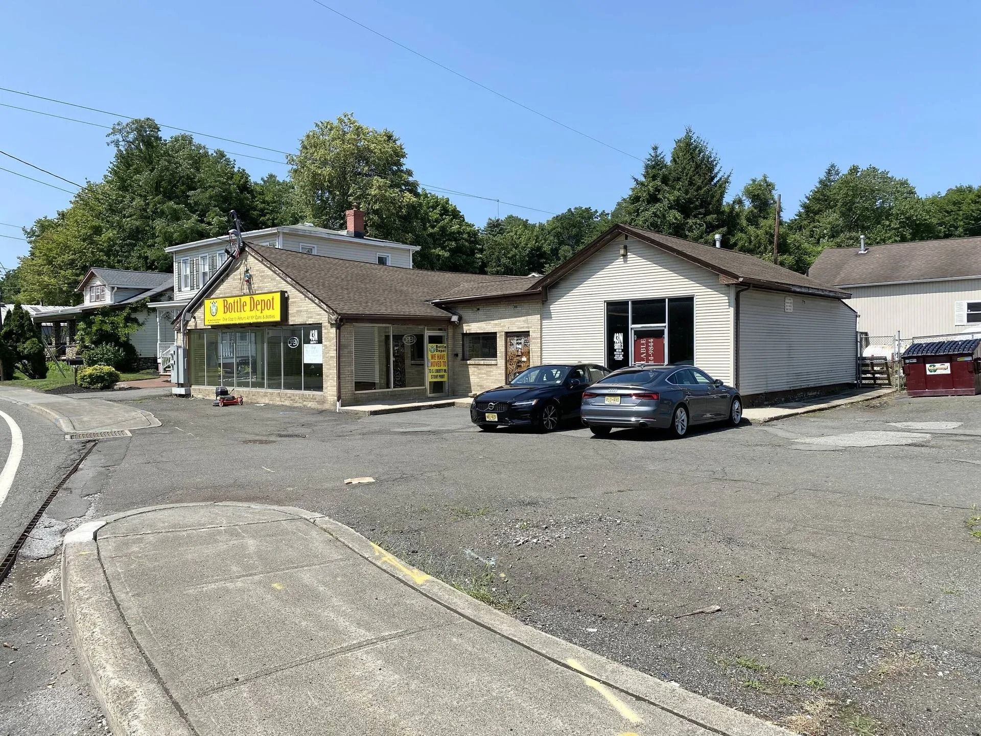 Small roadside store with yellow awning, parked cars, and gravel lot under a clear blue sky