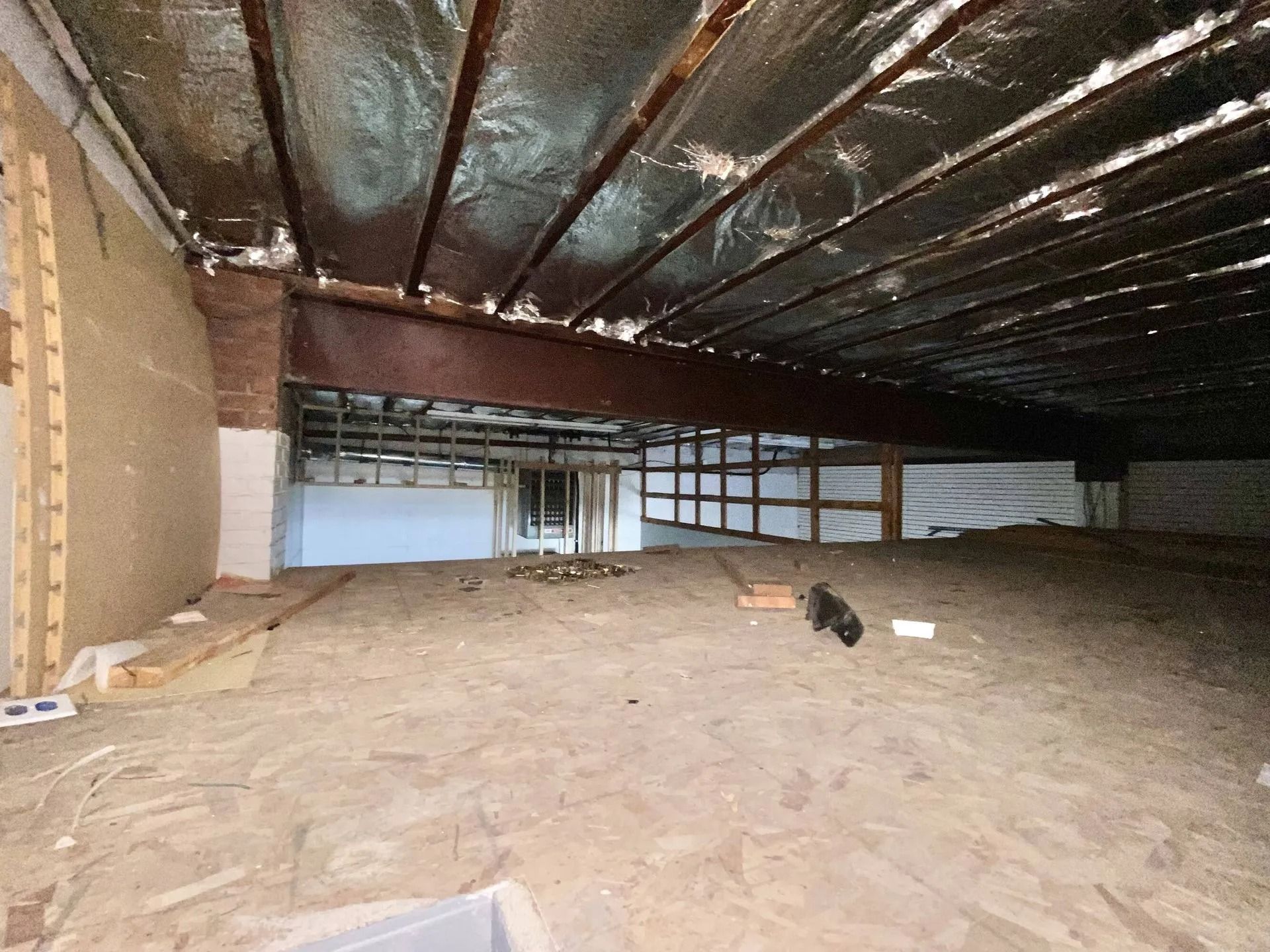 Empty attic with exposed rafters, insulation, and unfinished plywood flooring.