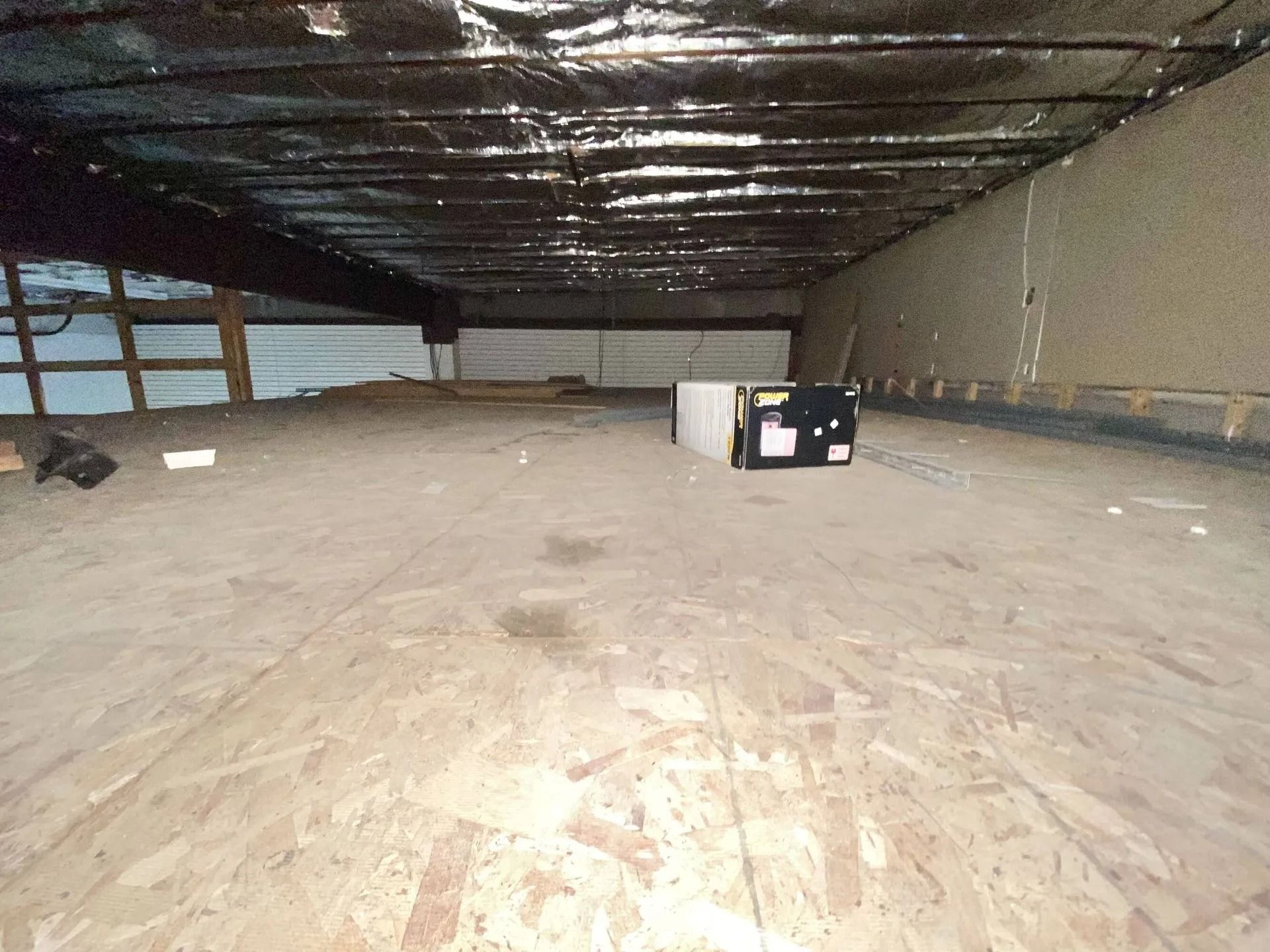 Empty unfinished room with exposed insulation, concrete floor, and a few scattered boxes.