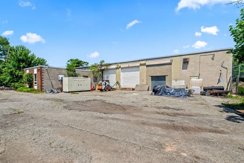 Industrial building exterior with scattered debris and gravel lot under a blue sky