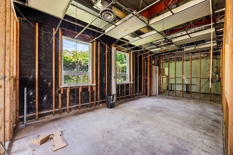 Unfinished interior room with exposed framing, ceiling ducts, and two open windows