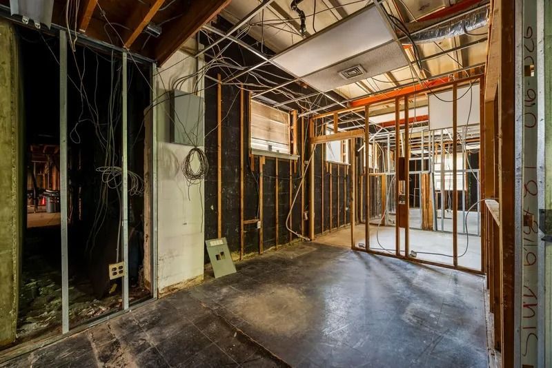 Partially demolished interior with exposed studs, wiring, and unfinished walls in a construction site