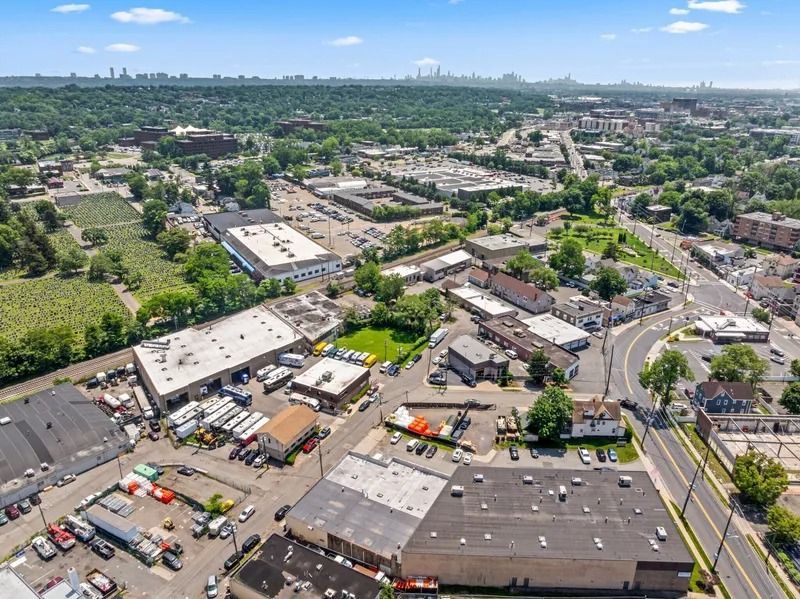 Aerial view of a suburban industrial area with warehouses, roads, parking lots, and distant city skyline