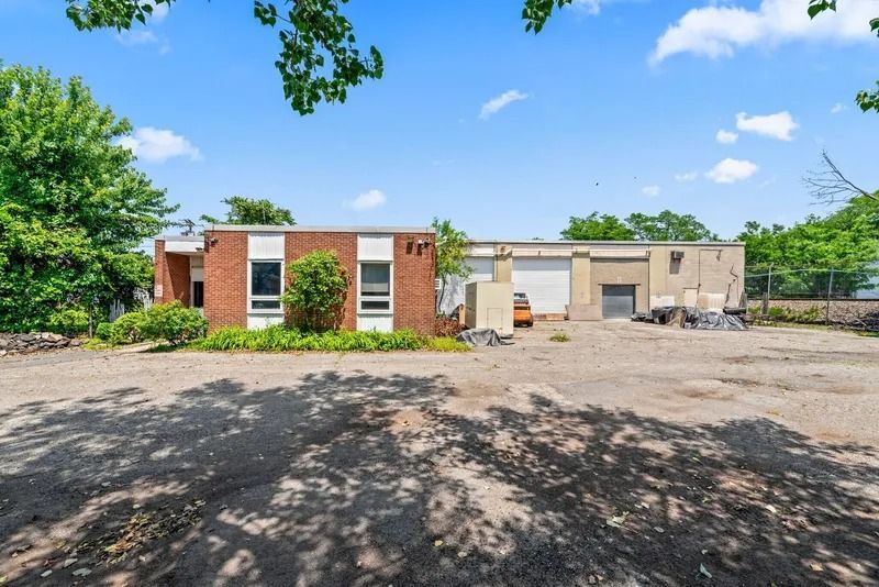 Brick commercial building with parking lot under a bright blue sky and trees nearby