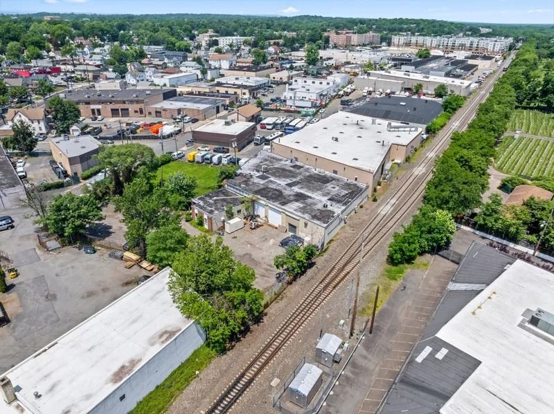 Aerial view of a small industrial neighborhood with warehouses, trees, and railroad tracks running through it
