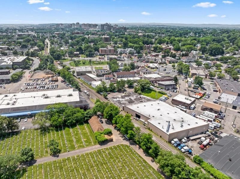 Aerial view of a suburban neighborhood with warehouses, rooftops, streets, and a cemetery in the foreground.