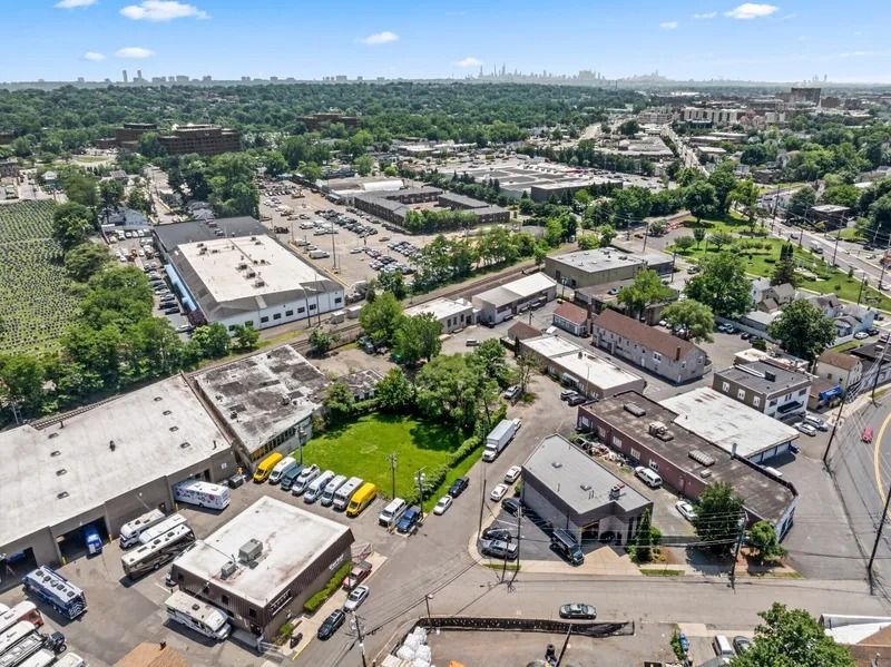 Aerial view of an industrial area with warehouses, parking lots, roads, and surrounding trees under a clear sky