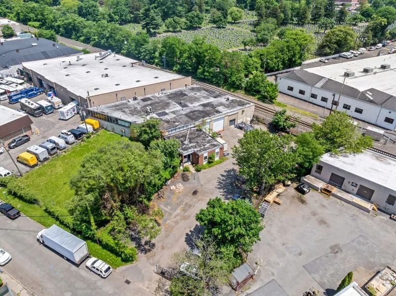Aerial view of an industrial complex with warehouses, parked vehicles, and trees surrounding the lot.