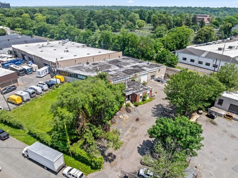 Aerial view of an industrial building, parking lot, and surrounding trees on a sunny day
