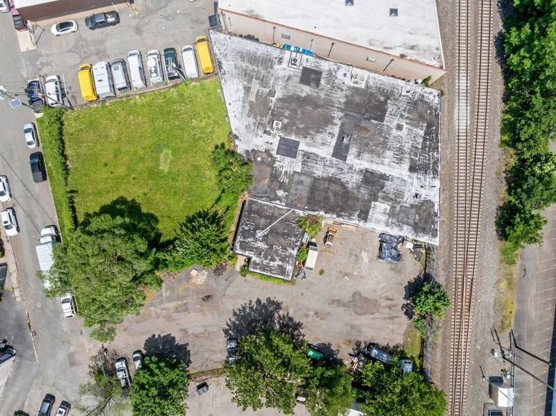 Aerial view of a vacant lot beside a weathered building, with parked cars and a road nearby.