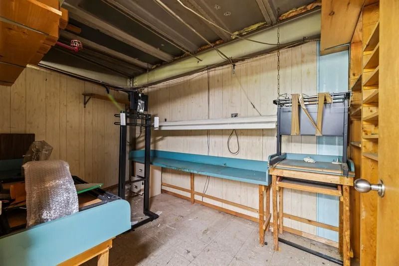 Workshop with wall-mounted workbench, pegboard, shelves, and a black metal machine near stacked materials.