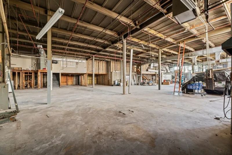 Empty industrial warehouse with exposed beams, concrete floor, and scattered equipment。