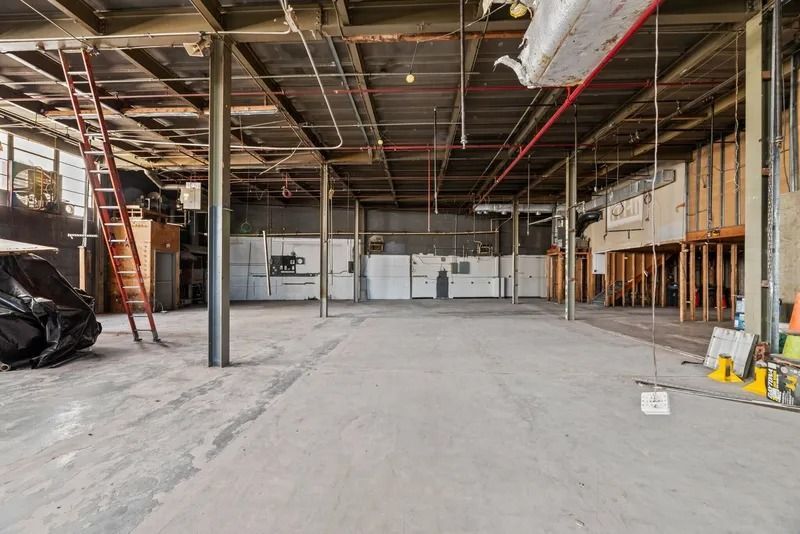 Empty industrial warehouse interior with exposed beams, concrete floor, and a ladder on the left