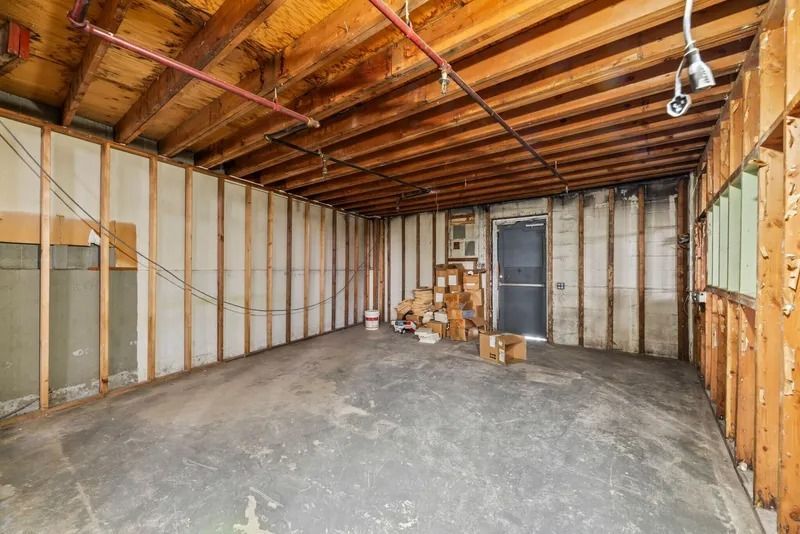 Empty unfinished basement with exposed framing, concrete floor, and scattered construction materials