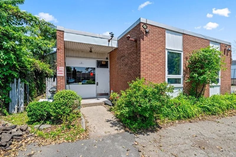 Brick apartment entrance with white door, windows, and green shrubs along a paved walkway