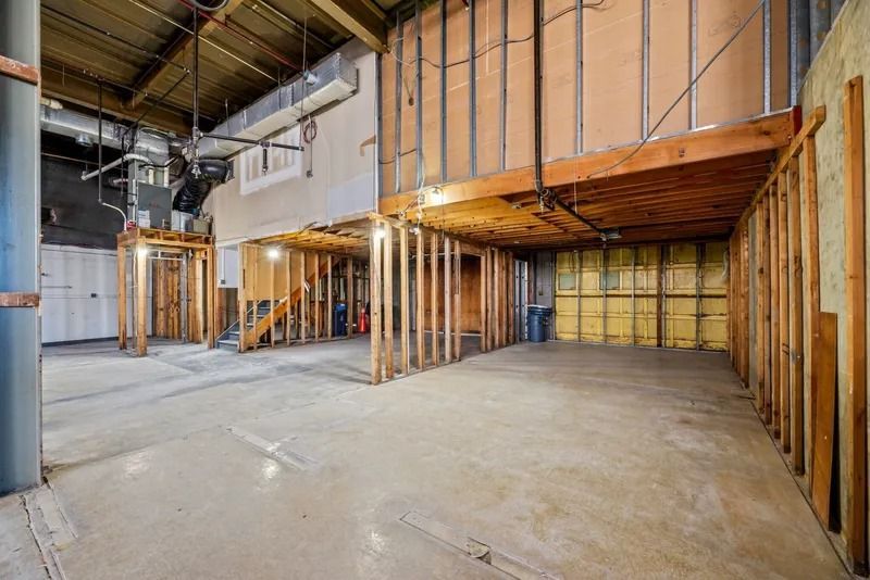 Unfinished basement interior with exposed wooden framing, concrete floor, and industrial ceiling beams
