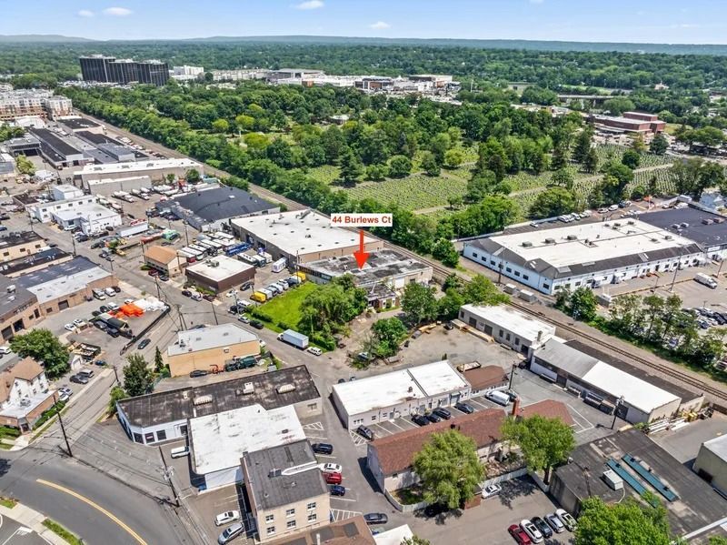 Aerial view of a suburban shopping center with parked cars, storefronts, and surrounding green trees.
