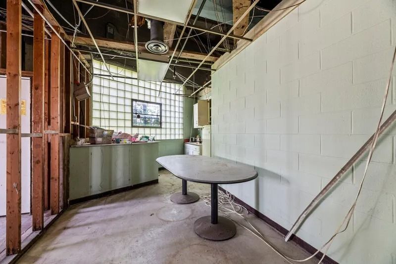 Empty unfinished room with exposed framing, white wall, and a small round table on a concrete floor.