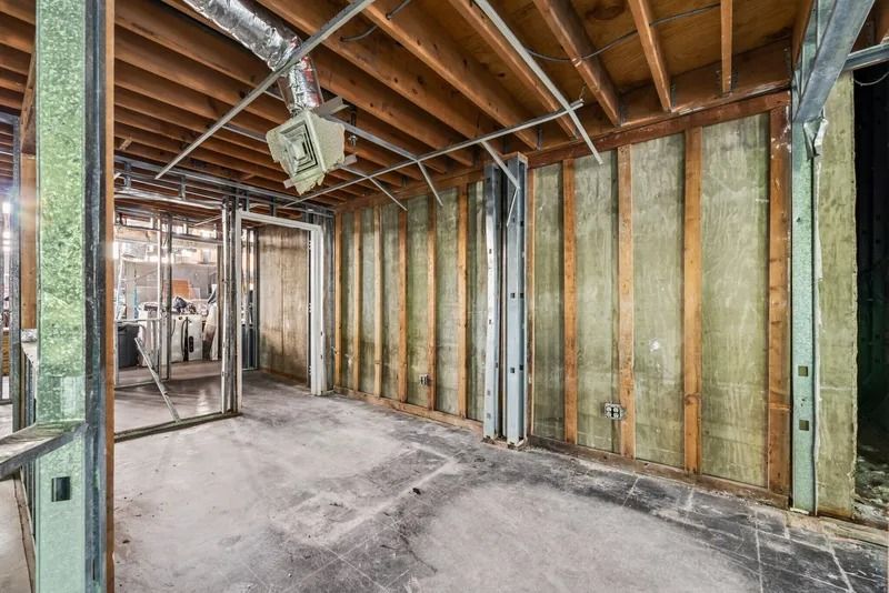 Unfinished basement with exposed wood framing, insulation, and concrete floor during renovation