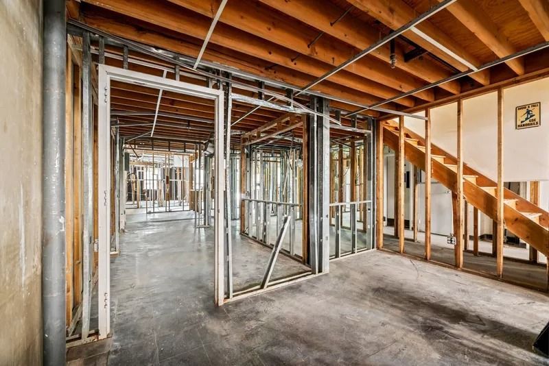 Unfinished basement interior with exposed wooden ceiling joists, metal studs, and concrete floor