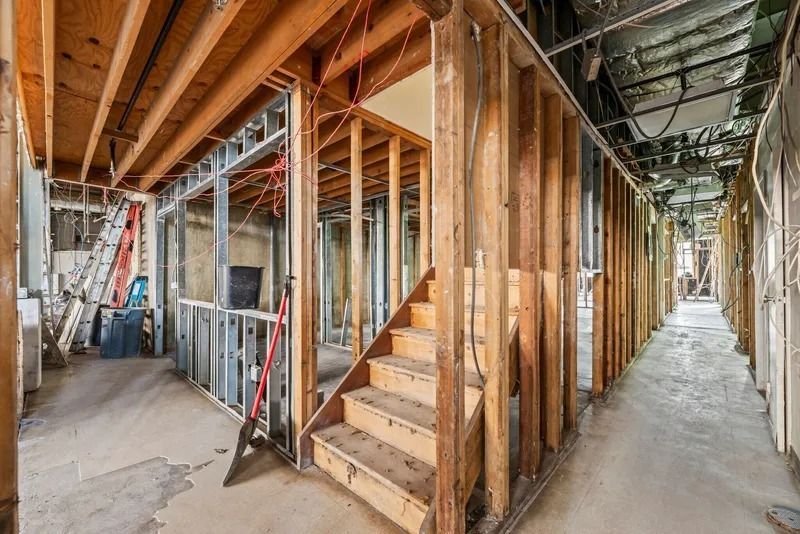 Unfinished building interior with exposed wood framing, stairs, and a long concrete hallway
