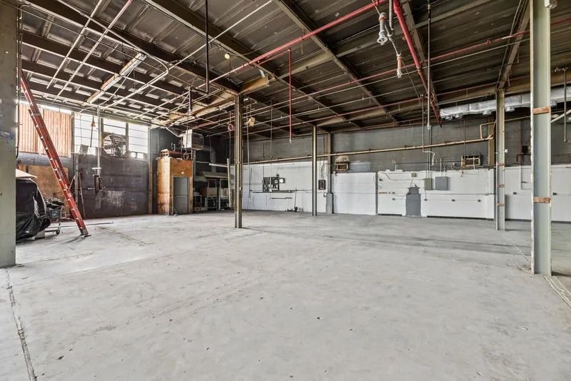 Empty industrial warehouse with concrete floor, exposed ceiling beams, and unfinished white walls