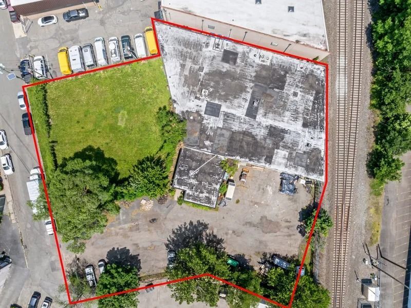 Aerial view of a lot outlined in red, with a grassy area, concrete building, and parked cars nearby