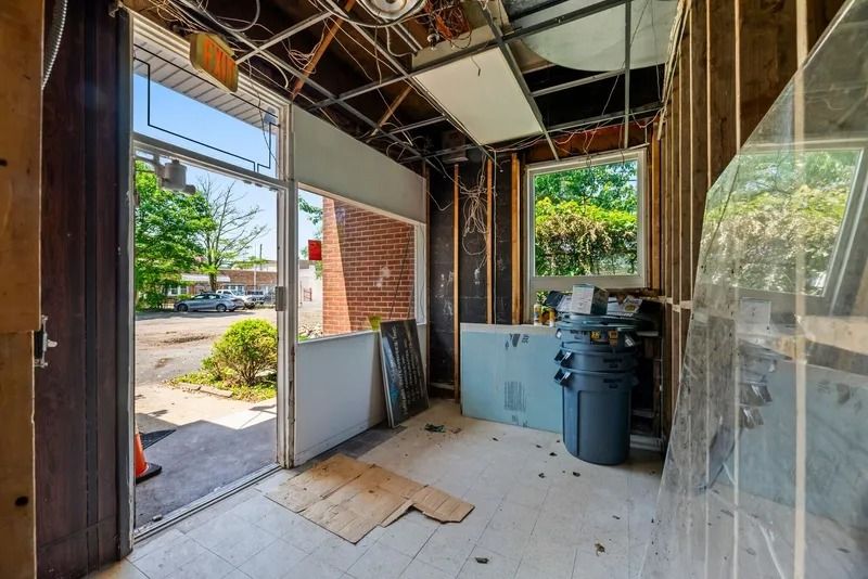 Empty industrial room with exposed beams, glass walls, and a blue appliance near the back.