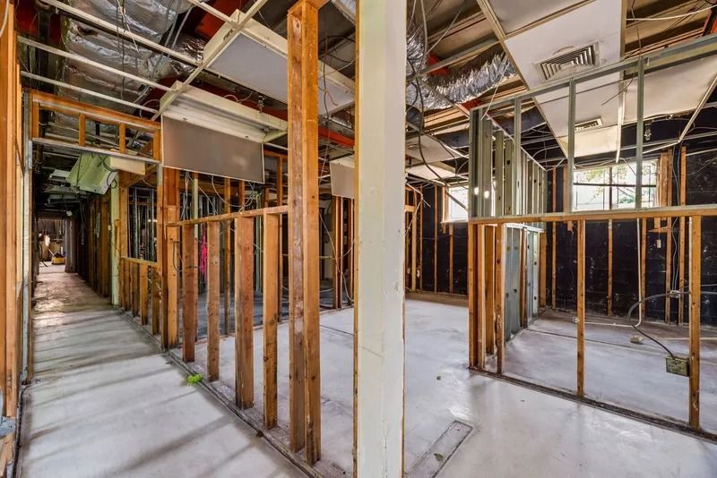 Interior construction site with exposed wooden framing, steel beams, and unfinished walls and floor