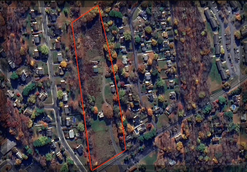 Aerial view of a suburban neighborhood with a red-outlined vacant lot among houses and autumn trees