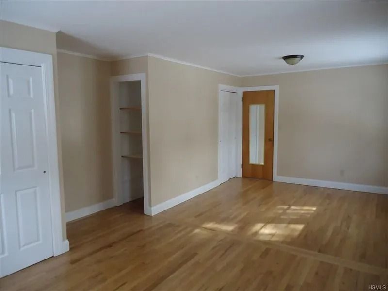 Empty beige room with hardwood floors, white doors, and a small closet alcove.