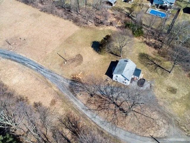 Aerial view of a small white house and driveway beside a curving road in a rural, grassy area.