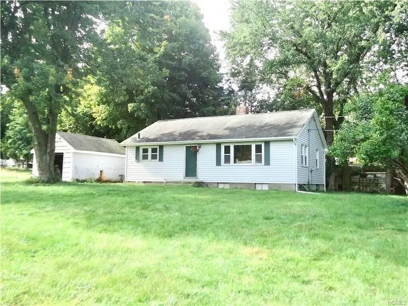 Small white house with green shutters and detached garage, surrounded by a large grassy yard and trees.