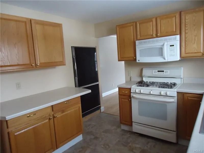Empty kitchen with wood cabinets, white appliances, and a gray floor.