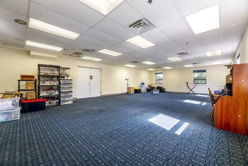 Empty carpeted office room with shelves, cabinets, and fluorescent ceiling lights