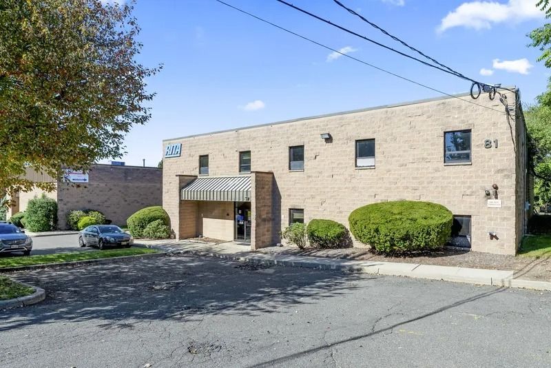 Brick office building with a covered entrance, parking lot, and trimmed bushes under a clear blue sky