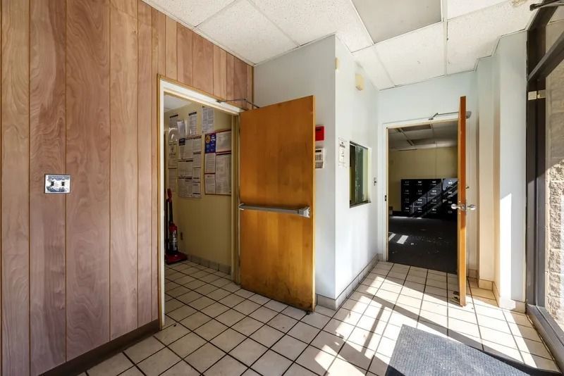 Open front door to a sunlit hallway with wood-paneled walls and tiled floor.