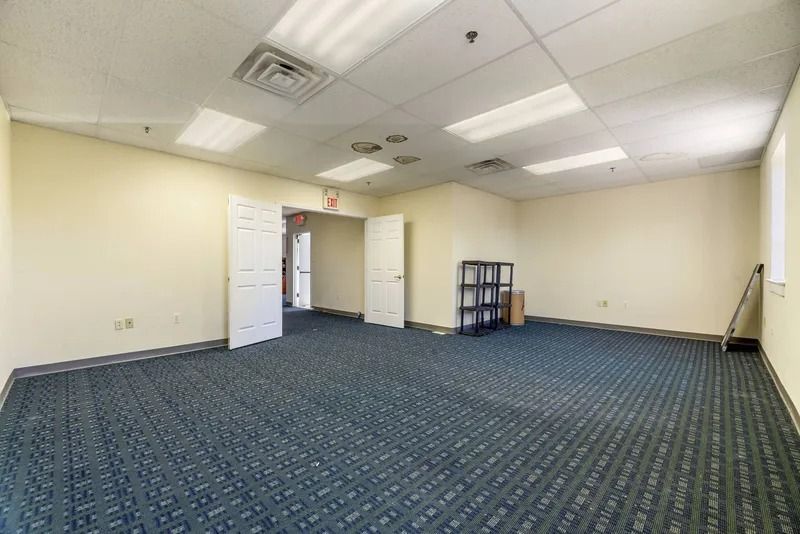 Empty office room with blue carpet, beige walls, fluorescent lights, and open door.