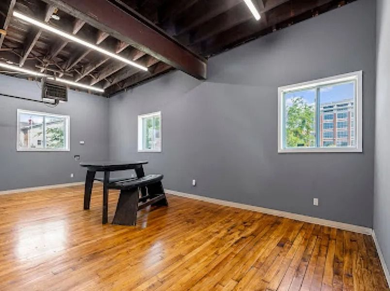 Empty room with wood floors, gray walls, exposed ceiling beams, and three windows.