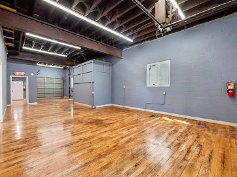 Empty industrial loft with polished wood floors, exposed beams, gray walls, and a red fire extinguisher.